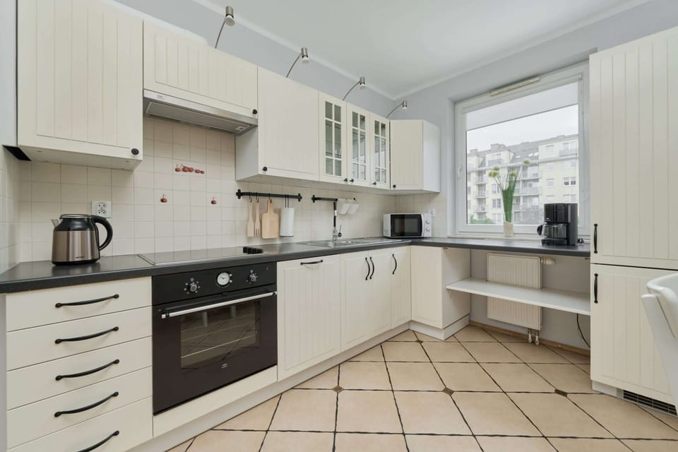 A spacious kitchen with classic white cabinetry, tiled flooring, and ample natural light, offering a functional cooking space.

