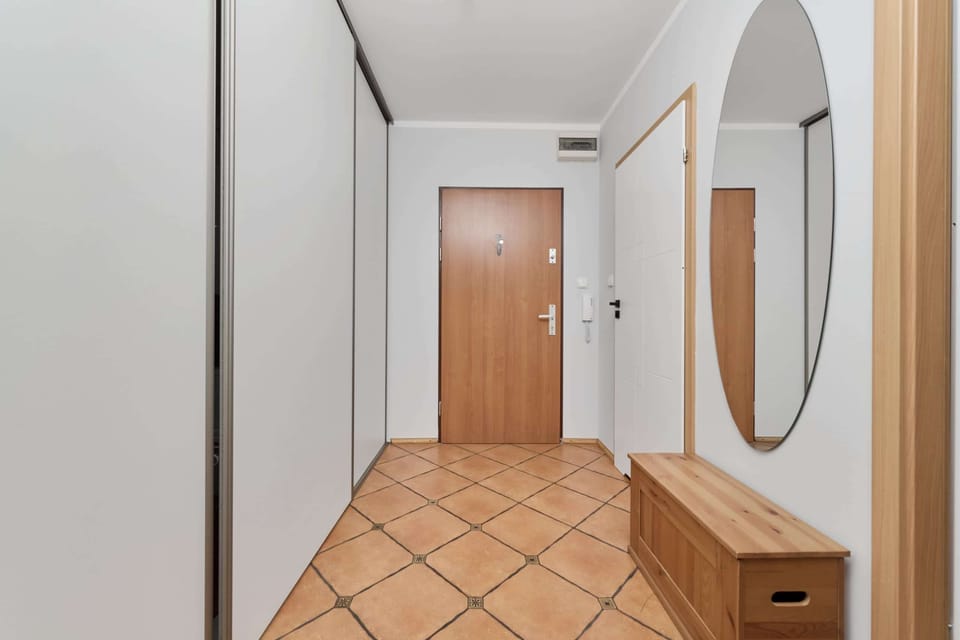 A welcoming hallway with tiled flooring, a wooden door, and a large mirror, creating a clean and inviting entrance.
