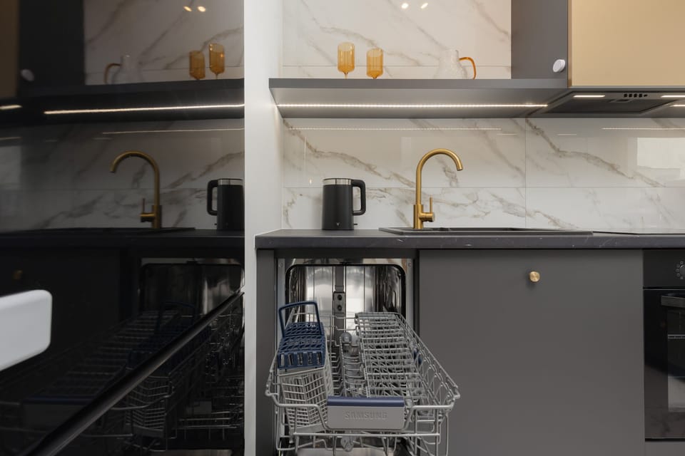 Kitchenette with dark furniture and high-quality appliances. There is an electric kettle on the black countertop.