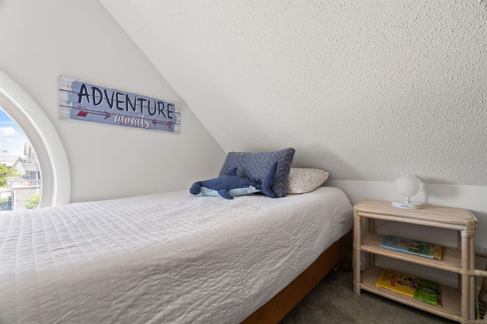 Cozy loft twin bed with a window framing sunset views over the street. A quiet, charming spot for kids to read, nap, or enjoy a peaceful retreat at Serenity Landing.