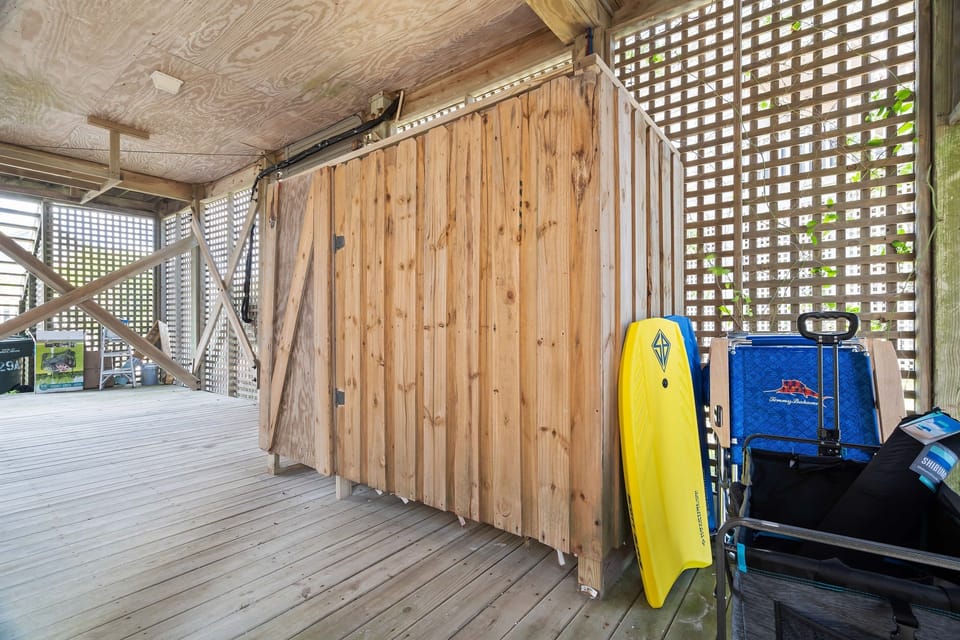 Carport-level shower area with guest beach gear neatly stored behind—boogie boards, chairs, beach cart, and toys. Everything you need for a fun, stress-free day at the sand and surf.