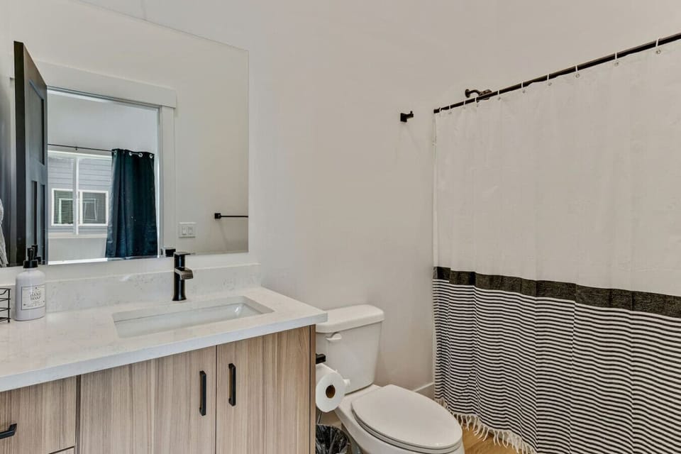 Stylish bathroom featuring a sleek vanity, large mirror, and shower/tub with a striped curtain 🚿🪞✨