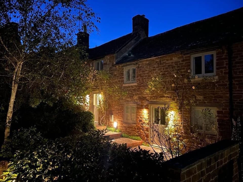 Warm sunset light falls across the front of Two Rose Walk Cottage, a classic Cotswold home near Daylesford. A peaceful first glimpse of this charming village cottage, perfectly placed for countryside walks, cosy pubs and relaxed evenings.