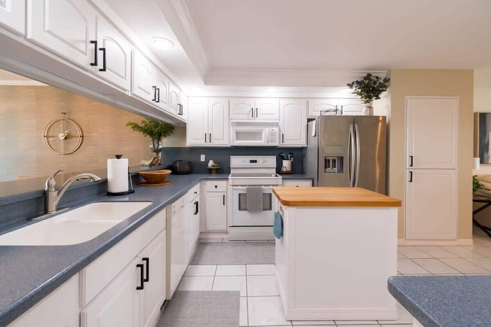 Modern kitchen with white cabinetry, stainless steel appliances, and a central island with a wooden countertop.