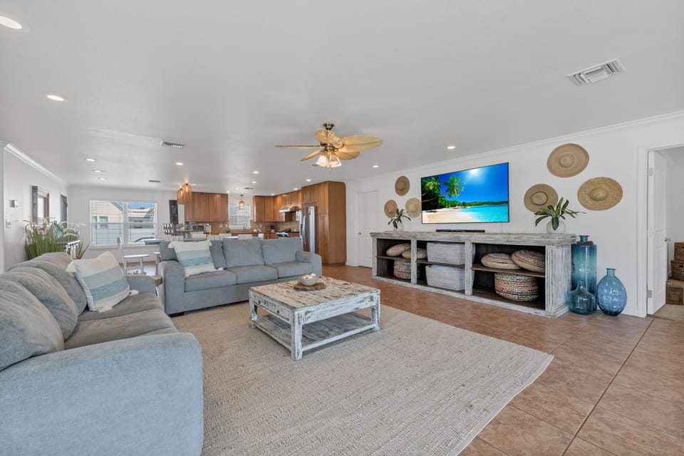 Sink into plush coastal comfort in this bright open-concept living space featuring ocean-blue sofas and tropical decor touches.