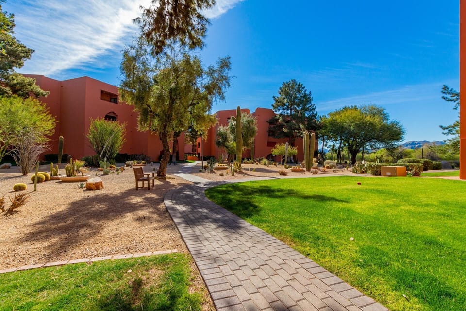 Curved gray paver walkway winds through green lawn and desert landscaping toward peach stucco condo buildings.