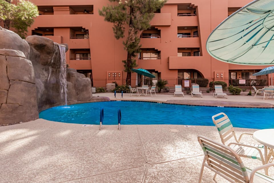 Curved pool with waterfall feature, surrounded by textured concrete deck and striped lounge chairs.