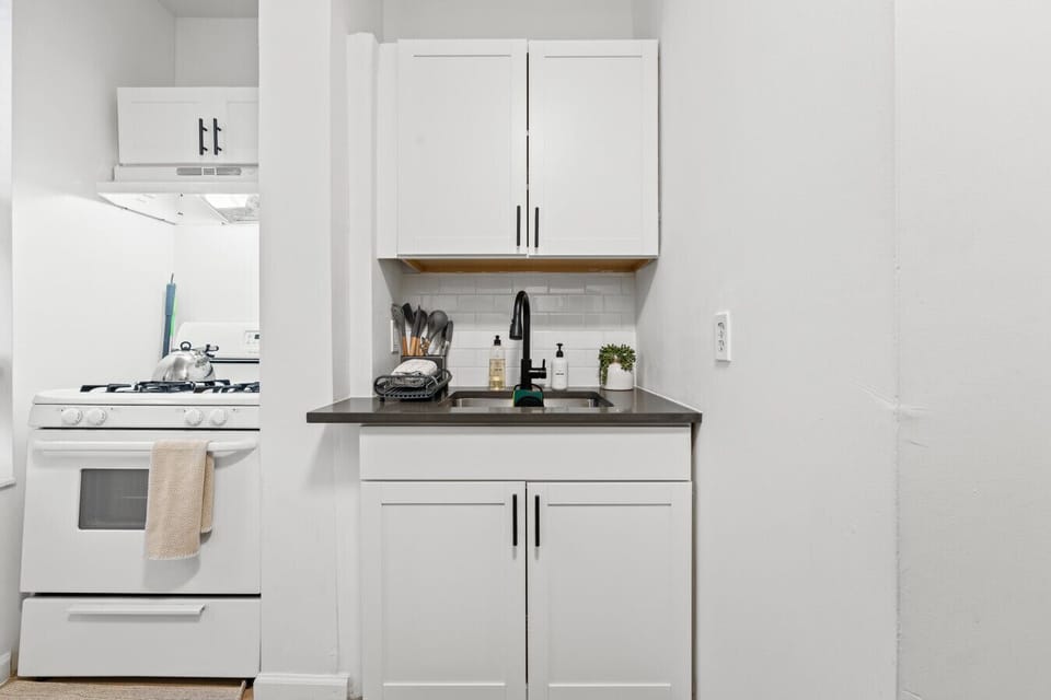 A tidy, fully stocked kitchenette featuring a gas stove, cooking tools, dish rack, soap station, and plenty of cabinet storage for a comfortable stay.