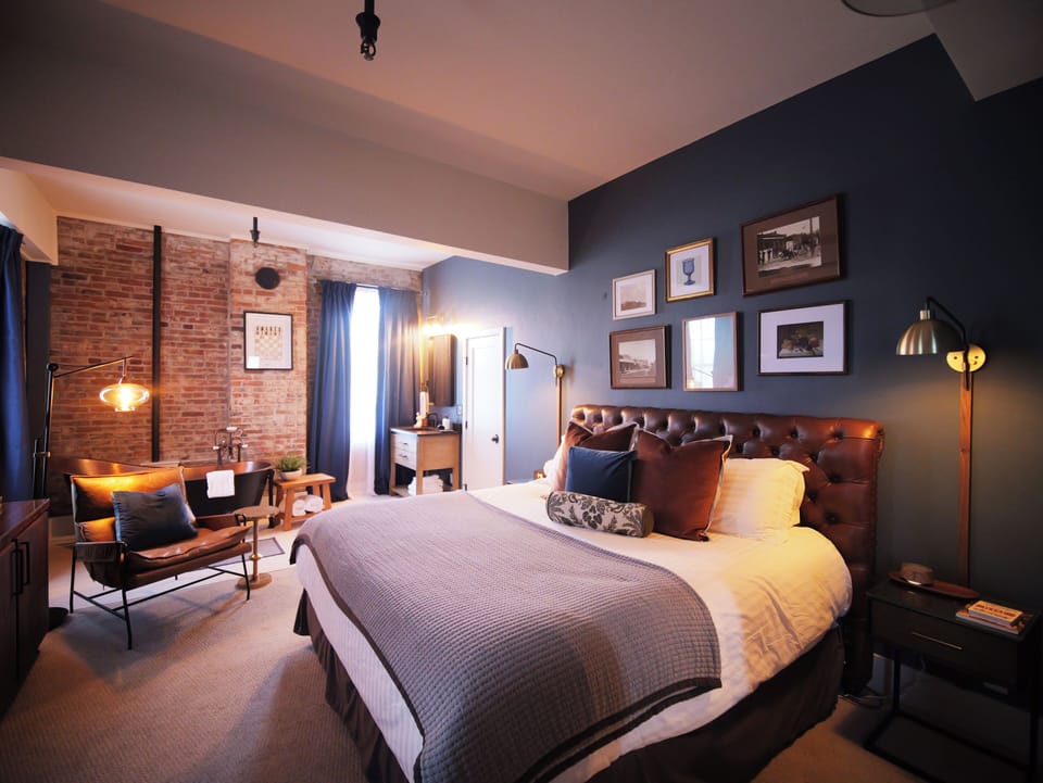 Elegant bedroom featuring a luxurious bed with tufted leather headboard, exposed brick accents, and cozy seating, creating a warm and inviting atmosphere.