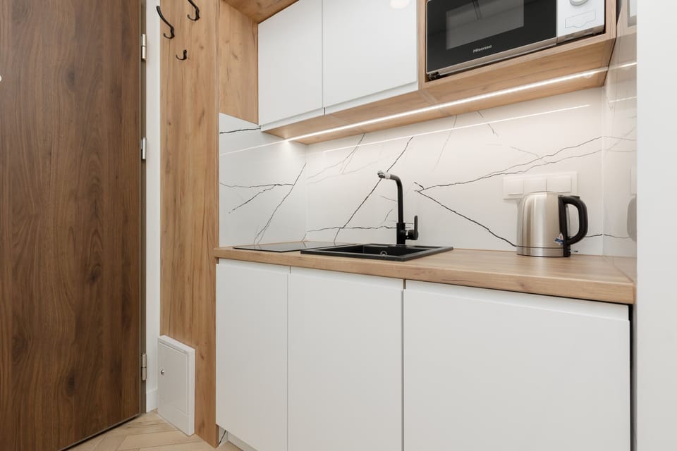 A modern kitchen corner with sleek white cabinets, a wooden backsplash, and a built-in microwave.
