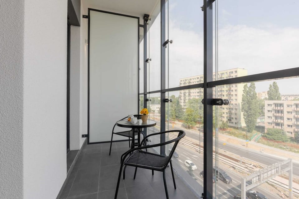 A private balcony with a small table and chairs, overlooking a modern residential complex.
