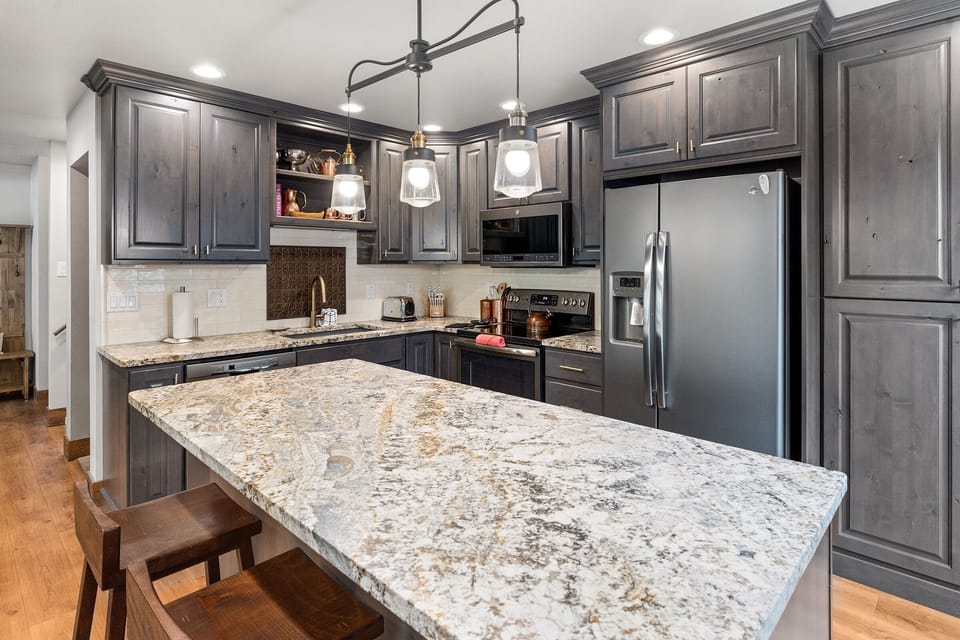 Large kitchen island, grey cabinets, brown stools.
