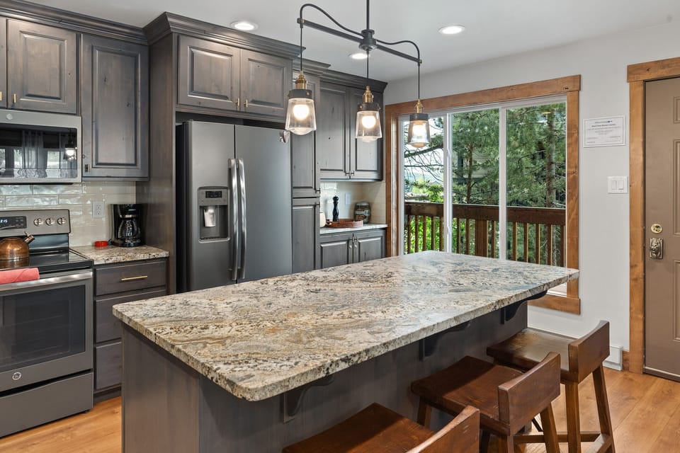 Large kitchen island with 3 stools, grey finishings, large windows.