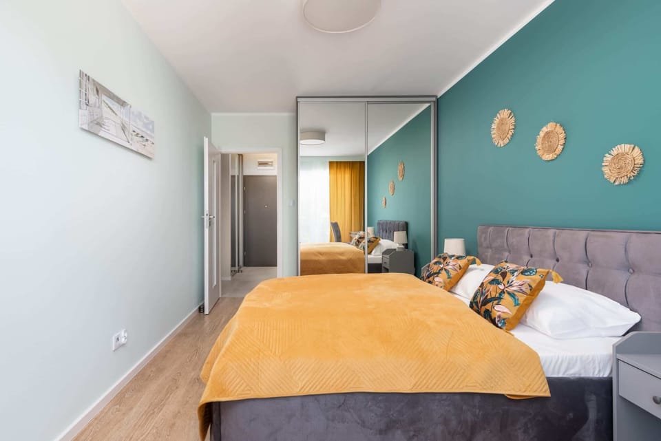 A cozy bedroom with a teal accent wall, a double bed covered with orange bedding, and decorative elements like golden wall hangings.