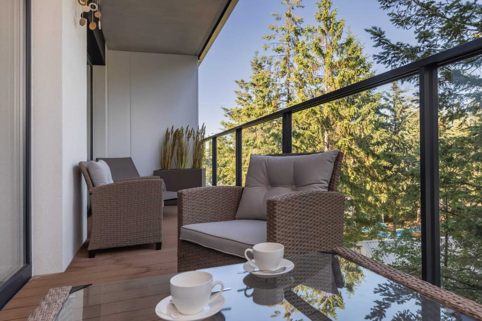 An outdoor seating area on a balcony, furnished with comfortable gray chairs and a table, surrounded by trees for a serene view.