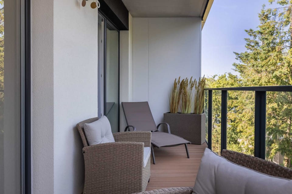 An outdoor seating area on a balcony, furnished with comfortable gray chairs and a table, surrounded by trees for a serene view.