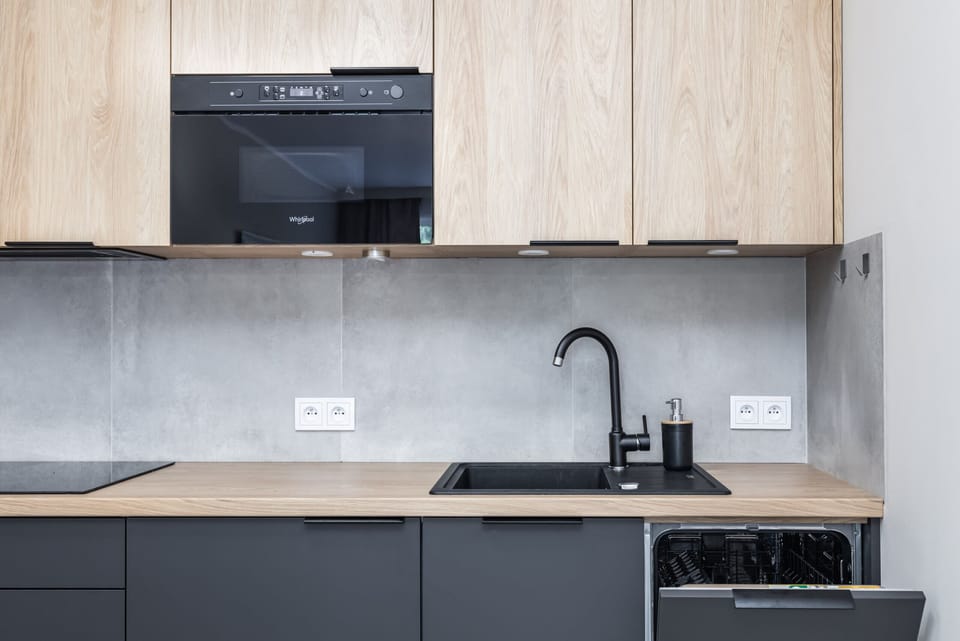 A minimalist kitchen with light wooden cabinets, black countertops, and integrated modern appliances.
