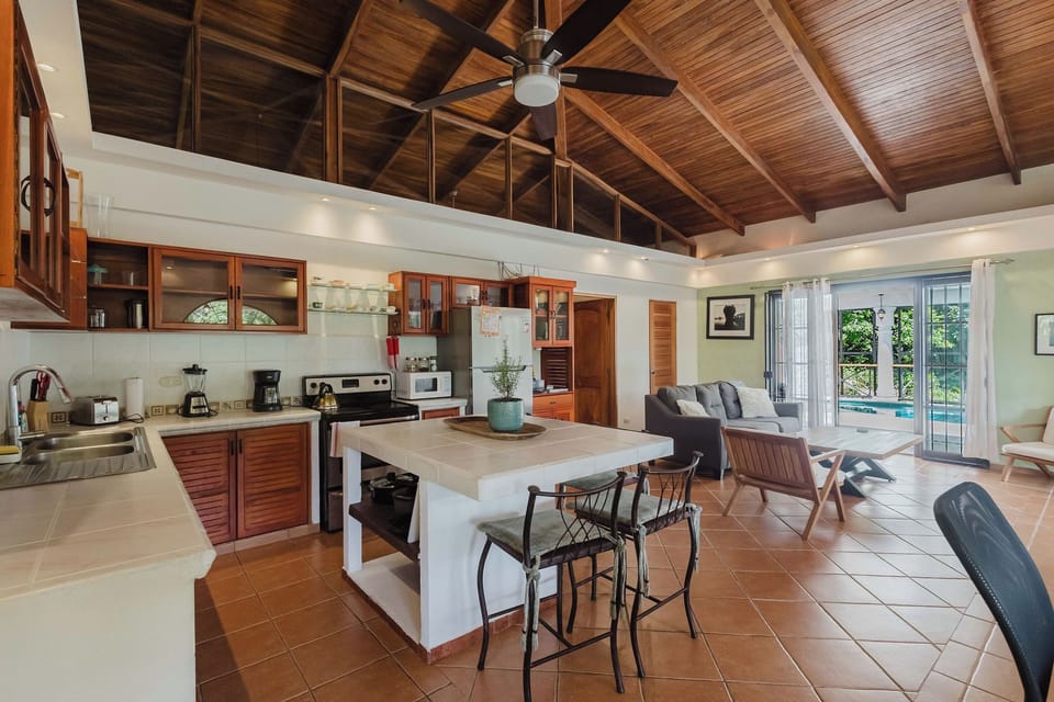 Open living area with vaulted wood ceilings, island seating, and garden views