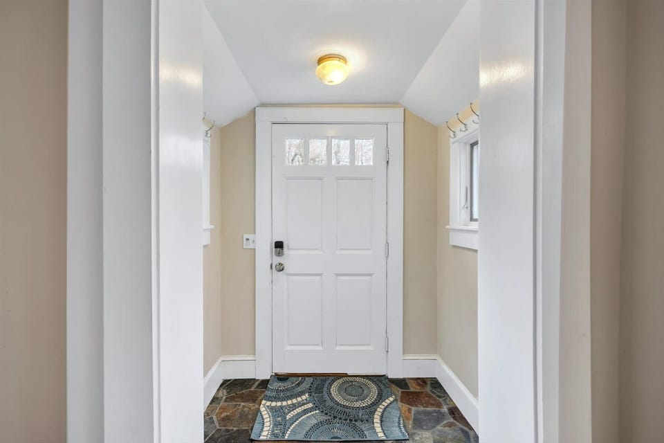 Entry with white glass-panel door, beige stone tile floor, colorful mat, and sidelights for natural light