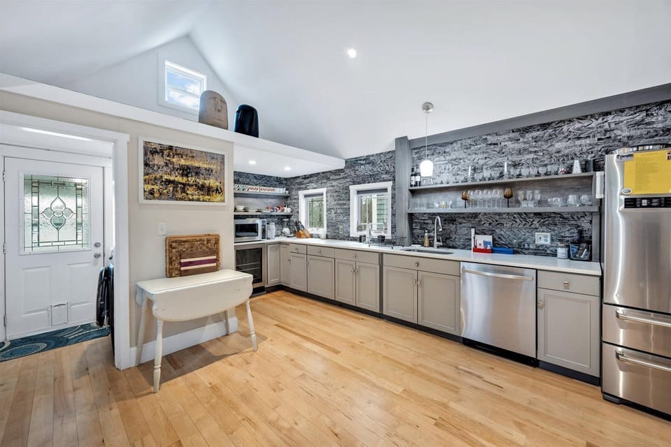 Kitchen with dark stone panels, gray cabinets, stainless fridge, microwave, and a white wooden-top table