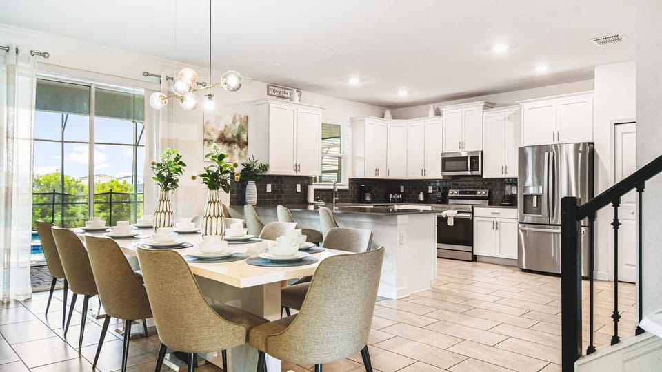 Elegant open kitchen and dining area with modern appliances, bright decor and pool view

