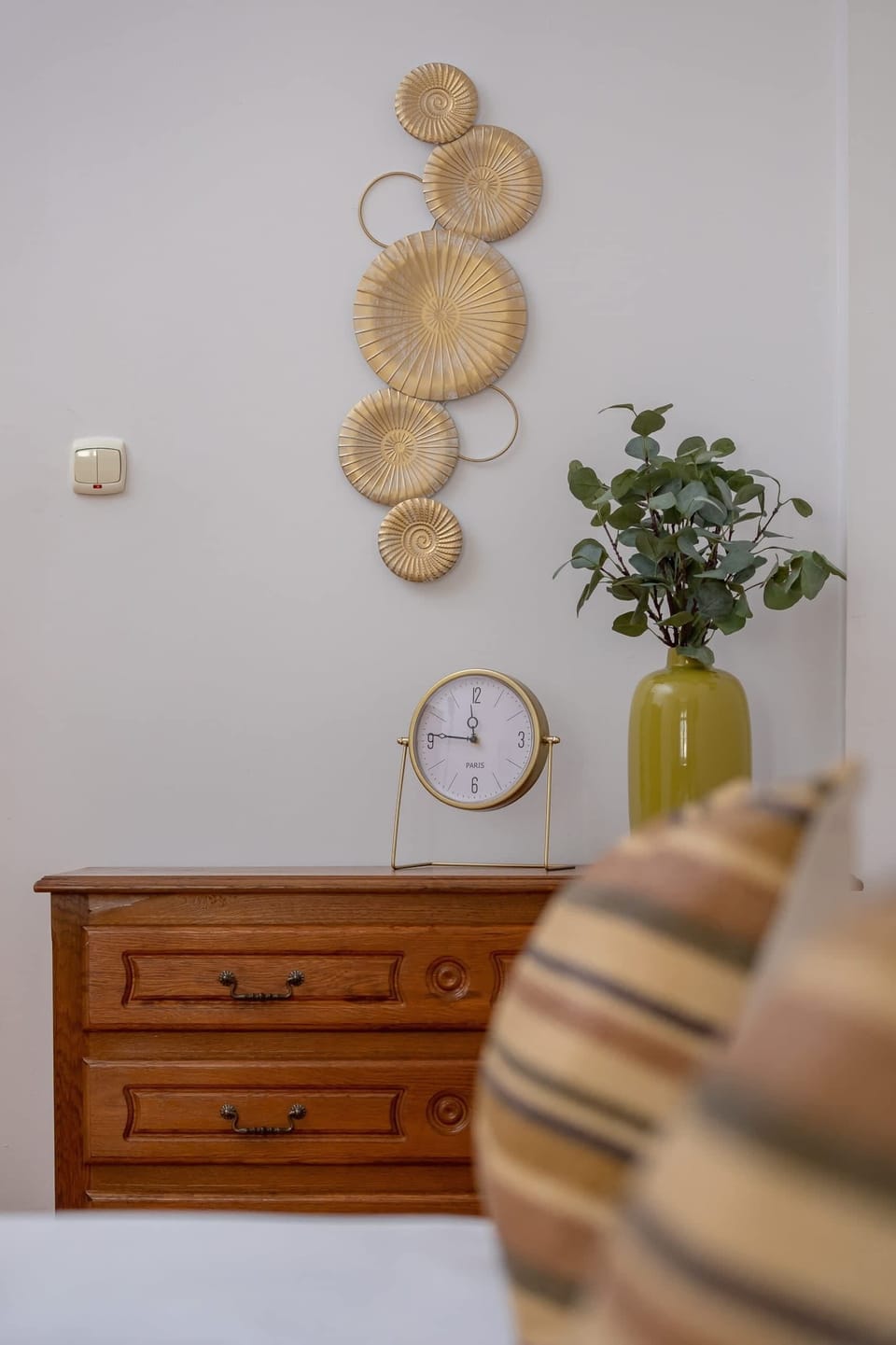 A small dresser with framed wall art and a decorative plant, creating a cozy corner.


