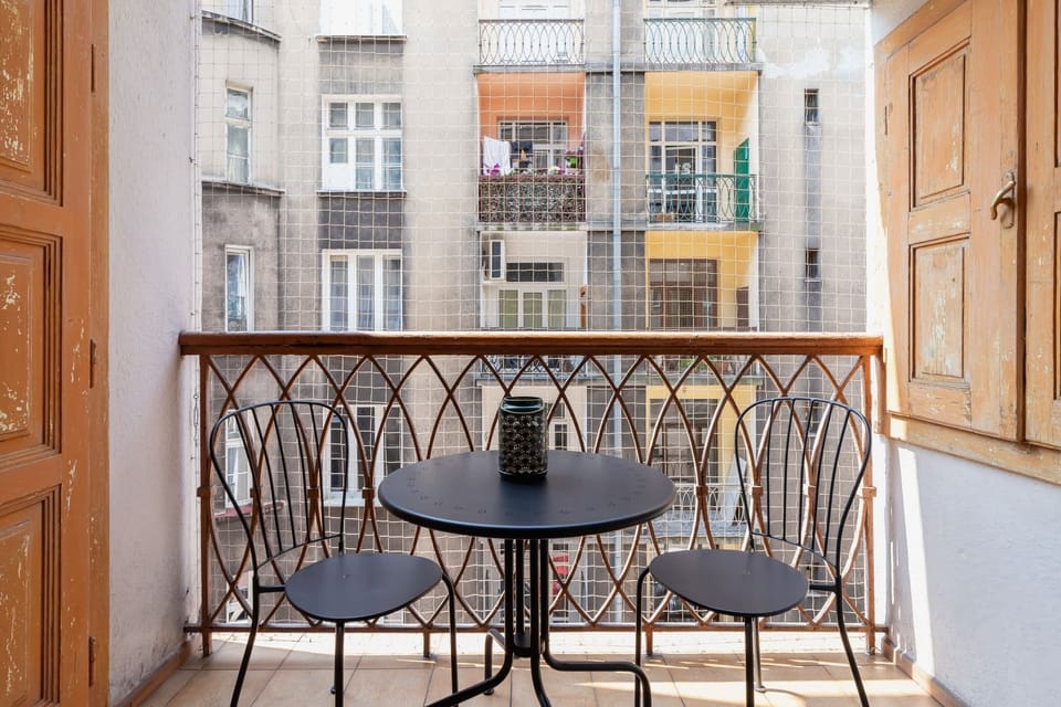 A balcony with a small table and chairs, overlooking a beautiful historical street.

