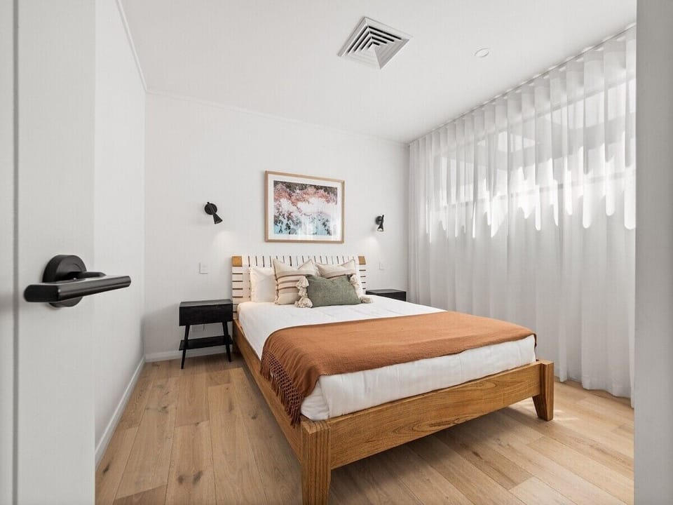 Chic second bedroom with a queen bed, soft lighting, and beautiful natural light through sheer curtains.