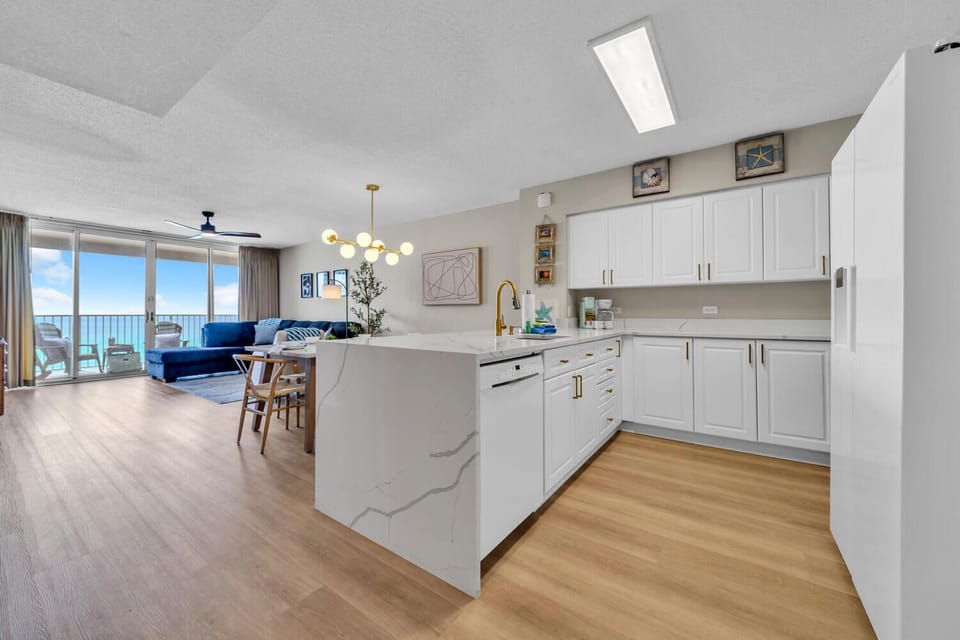 Your spacious kitchen island becomes the heart of coastal living, where morning coffee meets ocean breezes through floor-to-ceiling windows.