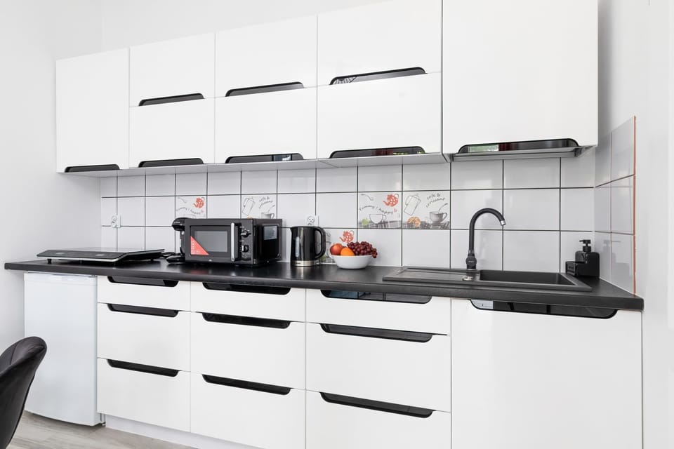 A modern kitchen with sleek white cabinets, black countertops, and a built-in microwave.

