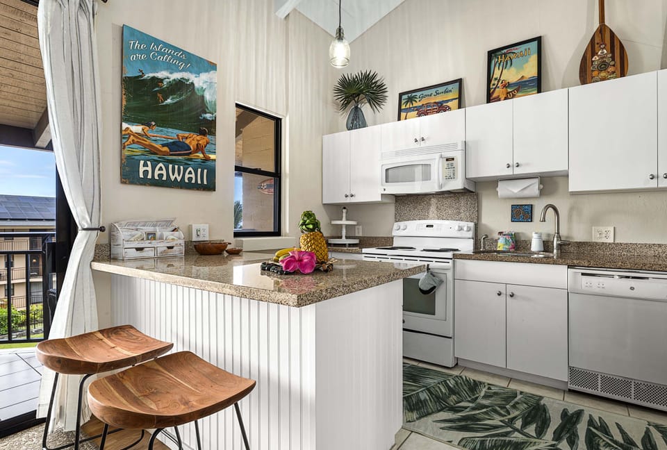 The upgraded kitchen features full-size appliances, ample cabinetry, and a convenient breakfast bar—perfect for preparing island meals and morning Kona coffee.