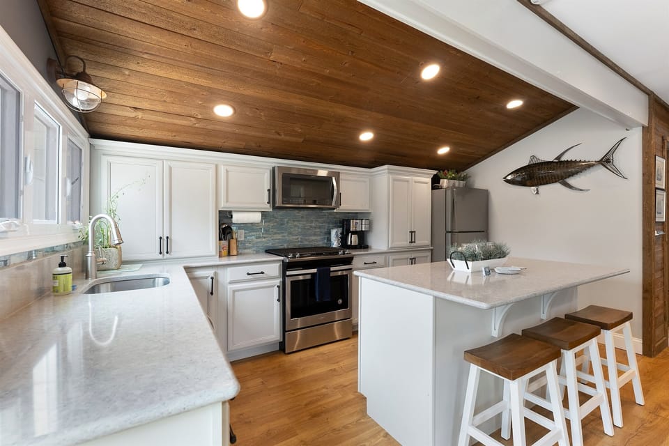 Stylish open kitchen w/ stainless appliances and wood-paneled ceiling.