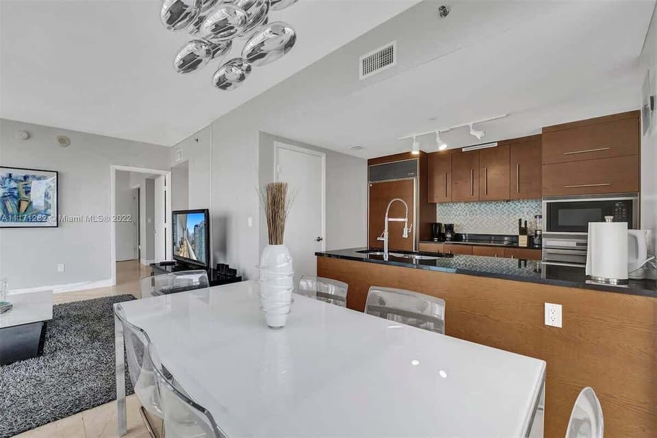 Open-concept dining and kitchen space with a bright white table, designer chandelier, and rich wood cabinetry. Seamlessly connected to the living area, it's perfect for entertaining or enjoying meals together.