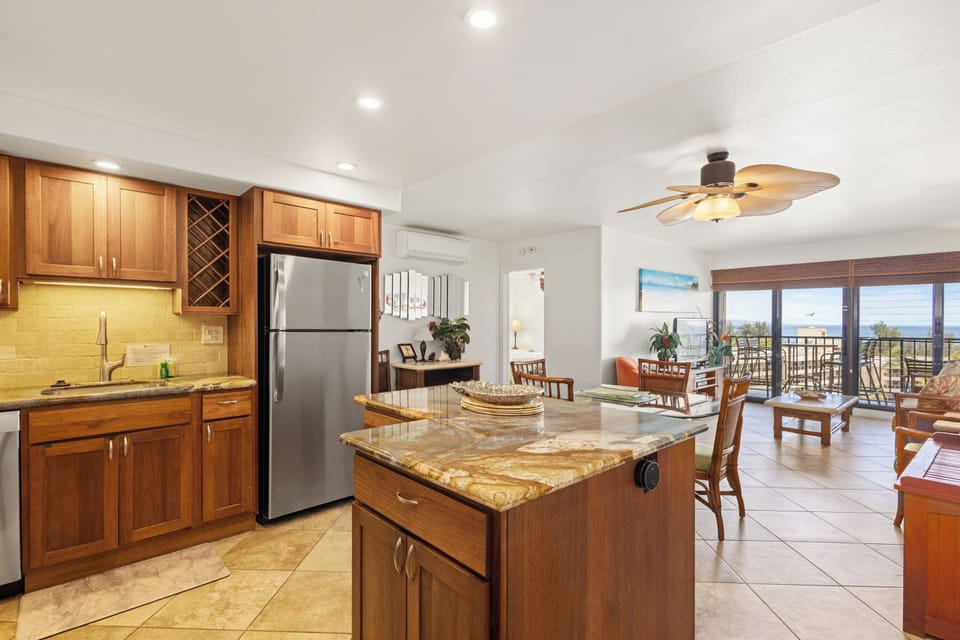 Bright, open-concept living awaits with island seating, a fully equipped kitchen, and coastal views through sliding doors. Cool tile floors and gentle ceiling fans ensure your comfort.