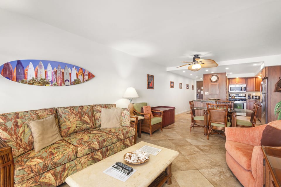 Relax in your spacious living area featuring tropical-inspired décor, comfortable seating, and a fully equipped kitchen. The island-style furnishings and ceiling fan create a welcoming beachside retreat.