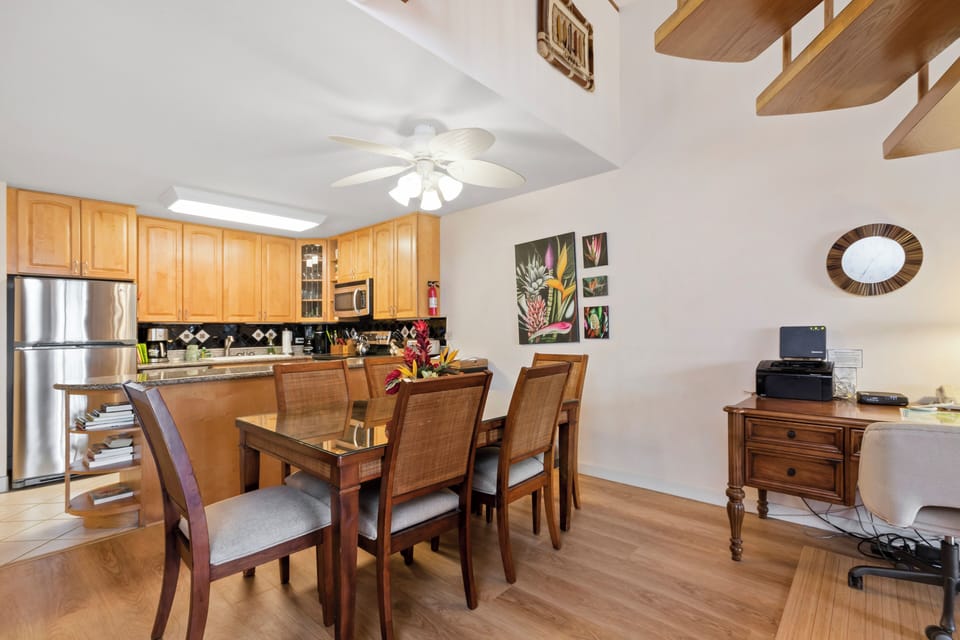 Settle into your bright open dining and kitchen area, with modern appliances, tropical artwork, and a fan overhead. Everything you need for a comfortable meal or casual workspace is right here.