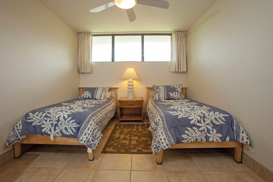 Your peaceful retreat features twin beds dressed in tropical-inspired linens, a bedside lamp for cozy reading, and a ceiling fan to keep you comfortable all night long.
