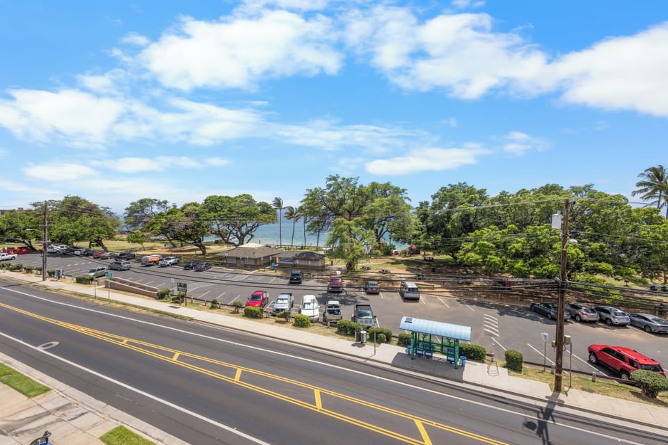 An elevated view showcasing the property's convenient location near coastal access, parking areas, and tree-lined streets with ocean views beyond.