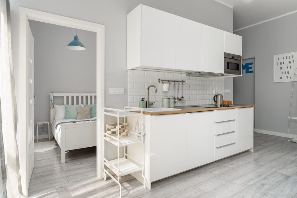 Compact open-plan kitchen with white cabinets and a sleeping area just behind, combining functionality with style.


