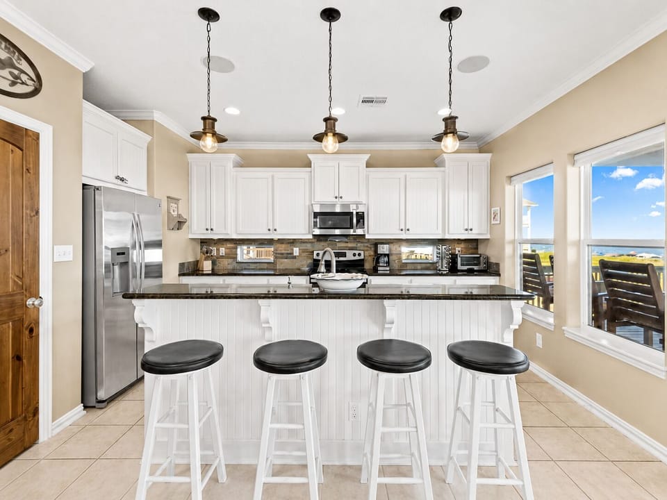 Spacious kitchen island with four bar stools, pendant lights, granite counters, stainless steel appliances, and generous meal-prep space.