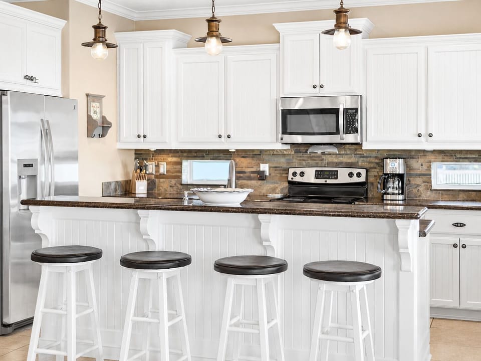 Fully equipped kitchen with white cabinetry, granite counters, stainless steel refrigerator, microwave, oven, cooktop, and breakfast bar seating.