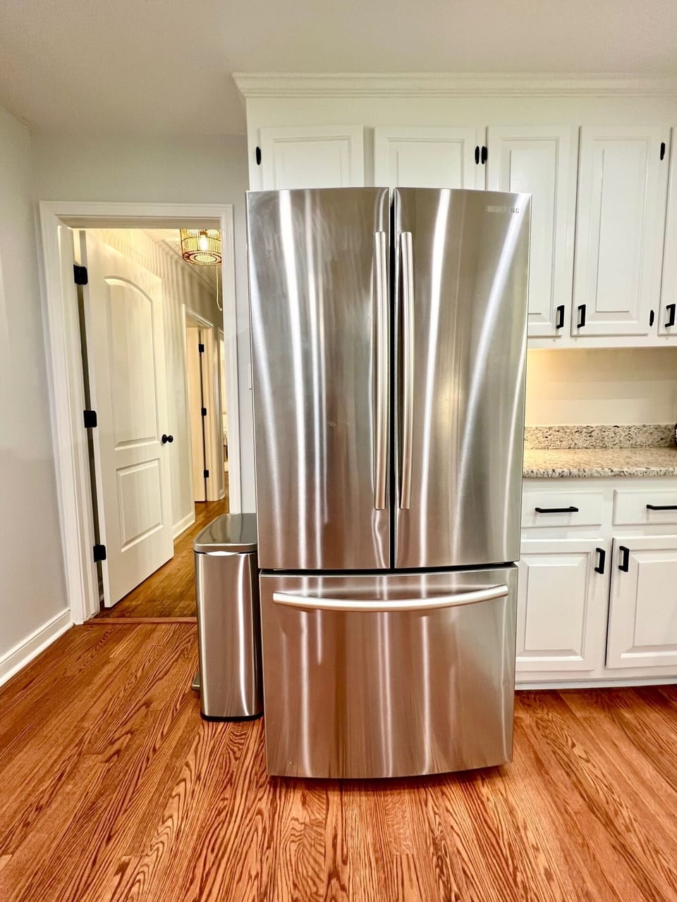 Stainless steel refrigerator with ice maker, with view of hall entrance to bedrooms with privacy door. 