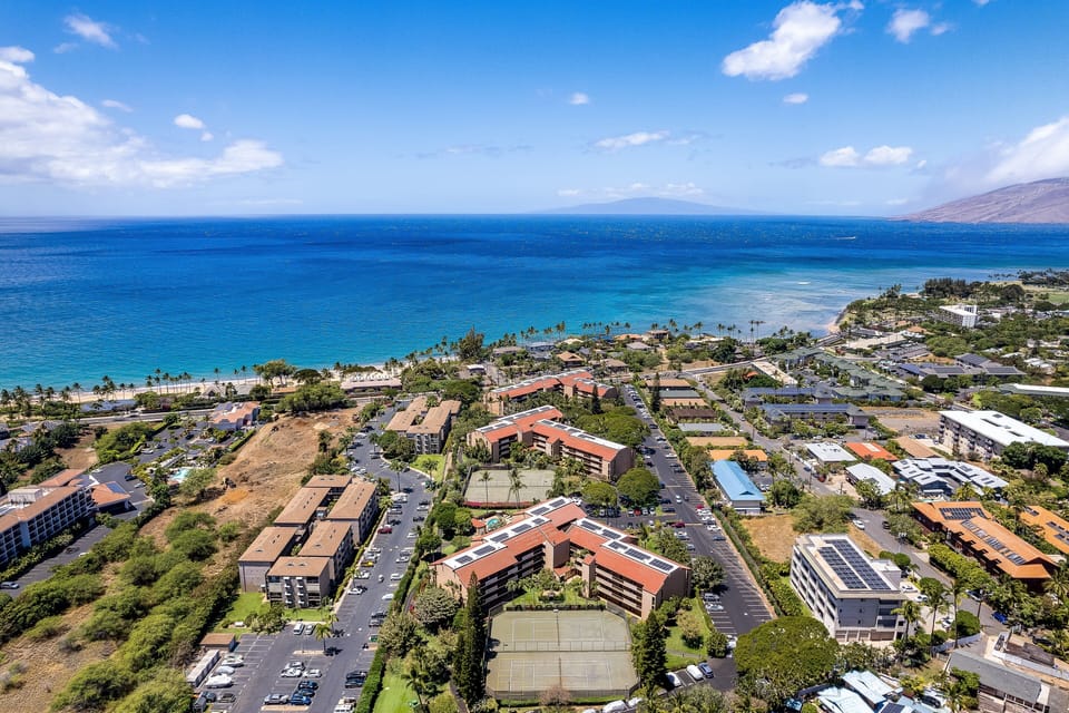 Bird's-eye view of paradise—tennis courts, lush greenery, and the ocean stretching beyond the horizon