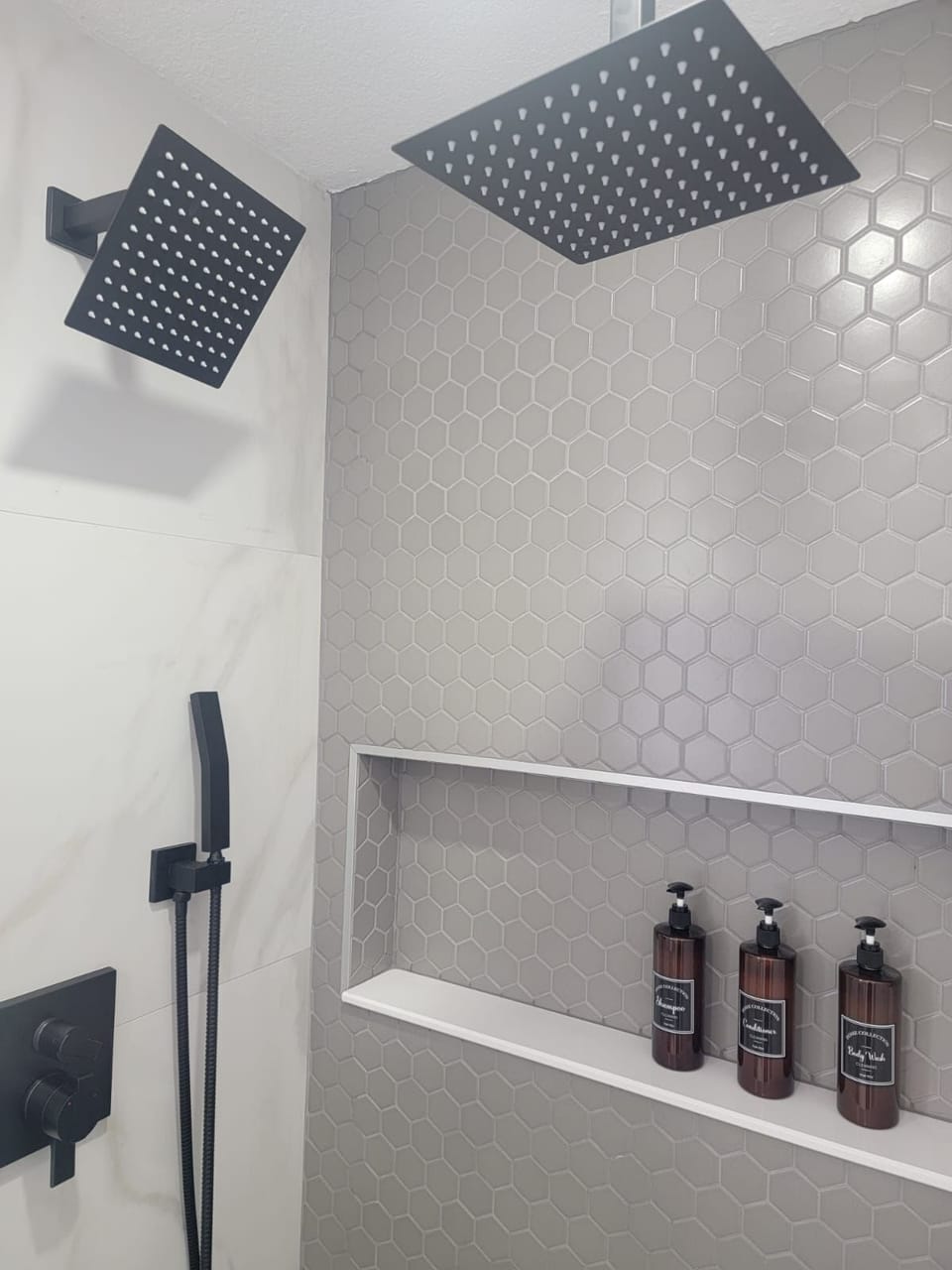 Modern shower with sleek tile design and amenities provided.