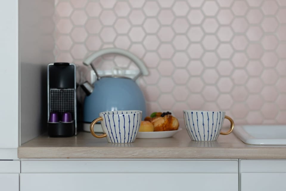 Close-up of a fully equipped coffee and tea station with a stylish pink backsplash.

