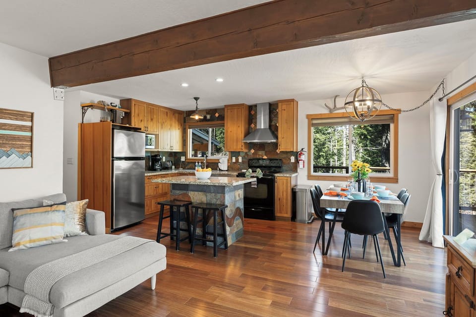 Your open-plan living space features warm wood beams, a fully equipped kitchen, and dining for six with forest views through large windows.