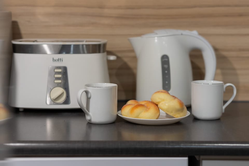 Close-up of a coffee and tea station with a kettle, toaster, and fresh breakfast setup.

