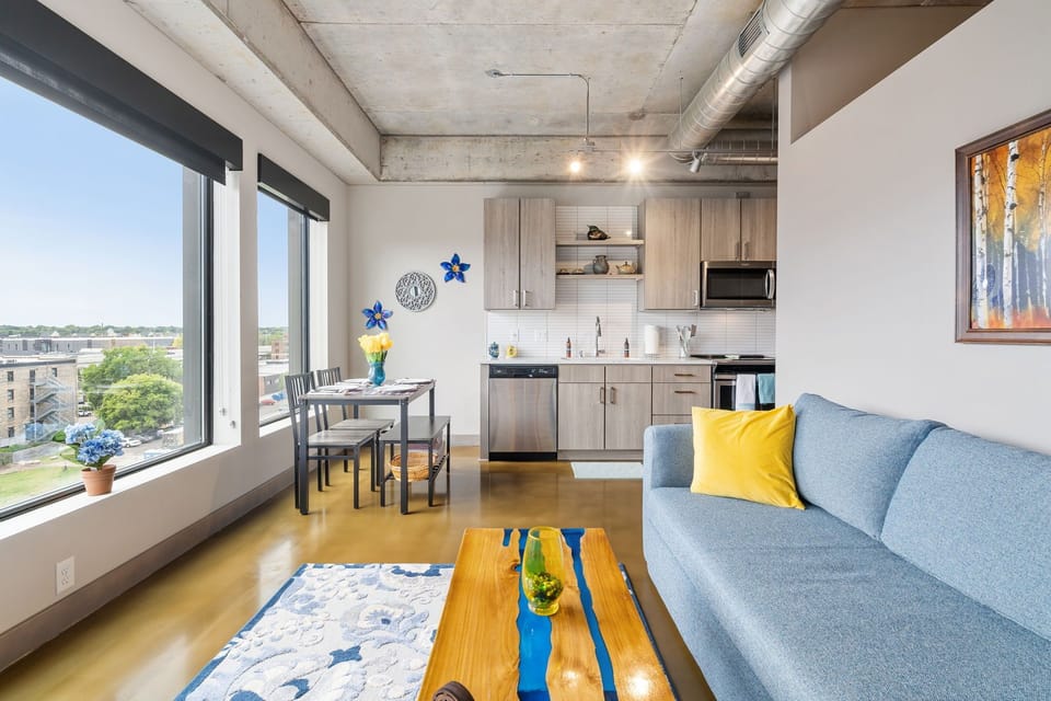 Unwind in your bright, modern loft with city views, cozy blue sofa, and fully equipped kitchen for memorable meals.
