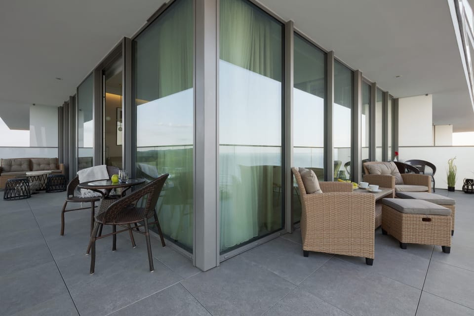 Large balcony with lounge furniture and glass railings, offering expansive views and outdoor relaxation space.

