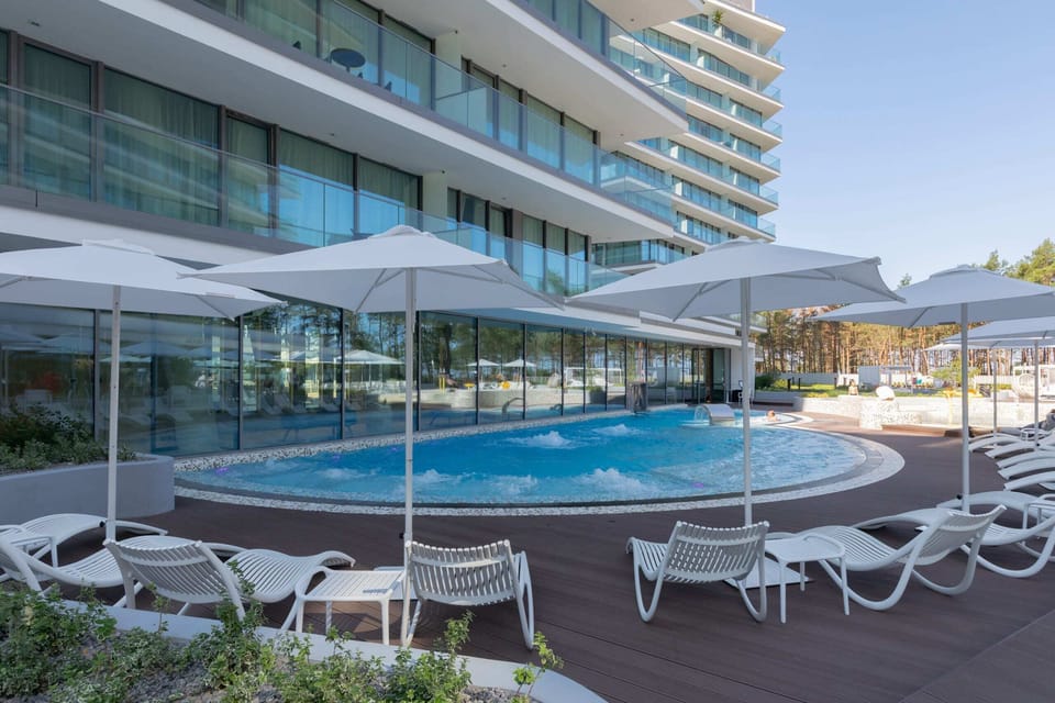 Contemporary outdoor pool area surrounded by sun loungers and a sleek apartment façade.

